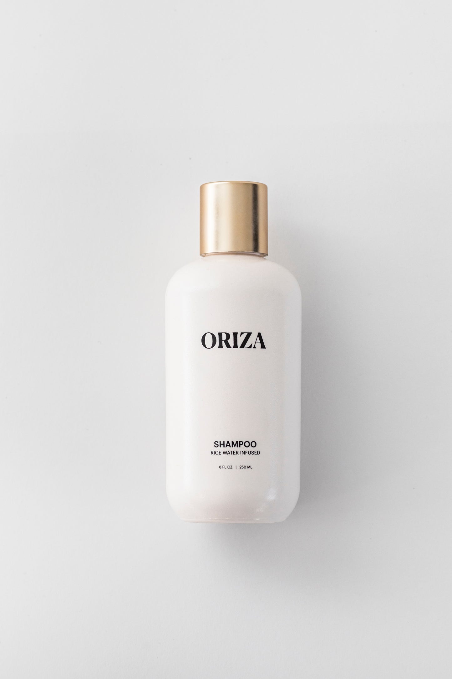 Oriza rice water infused shampoo in a sleek white bottle with a gold cap on a clean background.