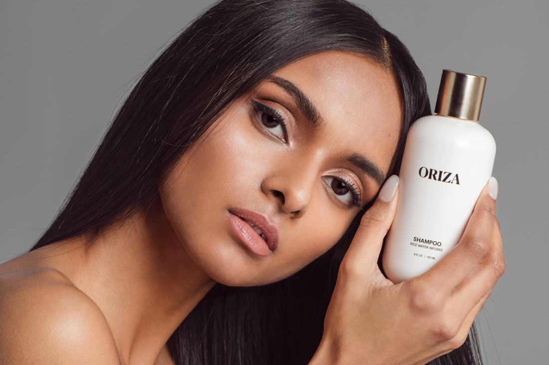 Model with long, healthy hair holding Oriza rice water shampoo
