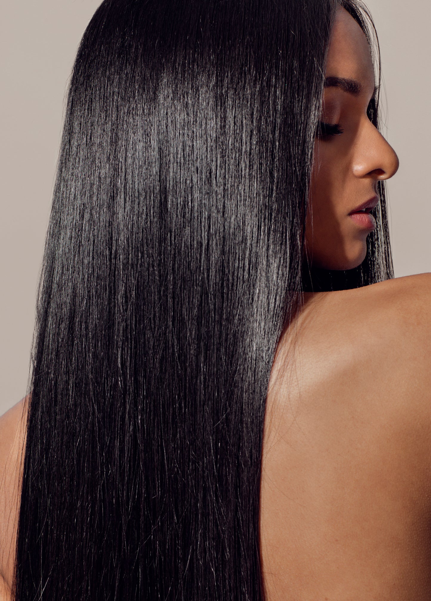 A woman with long, straight, glossy hair turned in profile, showcasing shine and smoothness achieved with Oriza Halo Oil.